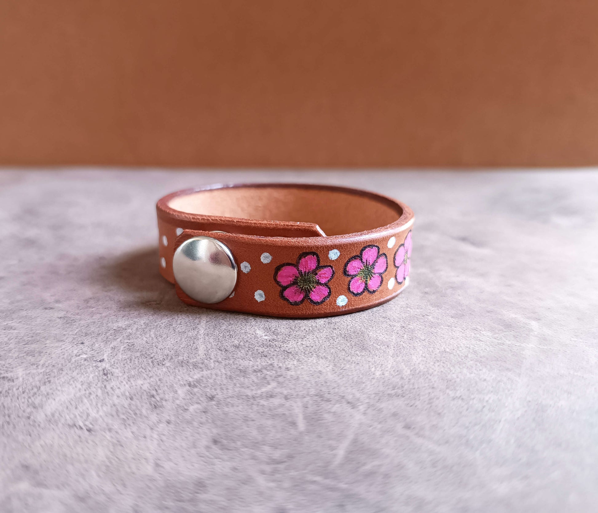 Leather bracelet with floral designs and a silver button on a light gray surface.