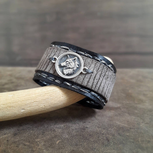 Gray woven bracelet with a silver wolf pendant on a wooden surface