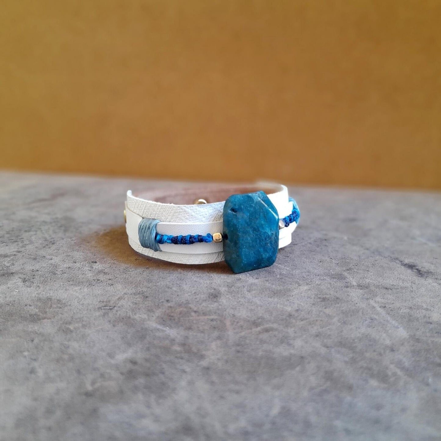 close-up side view of the large raw natural Apatite stone and the white bracelet, highlighting its vibrant blue hues and unique texture.