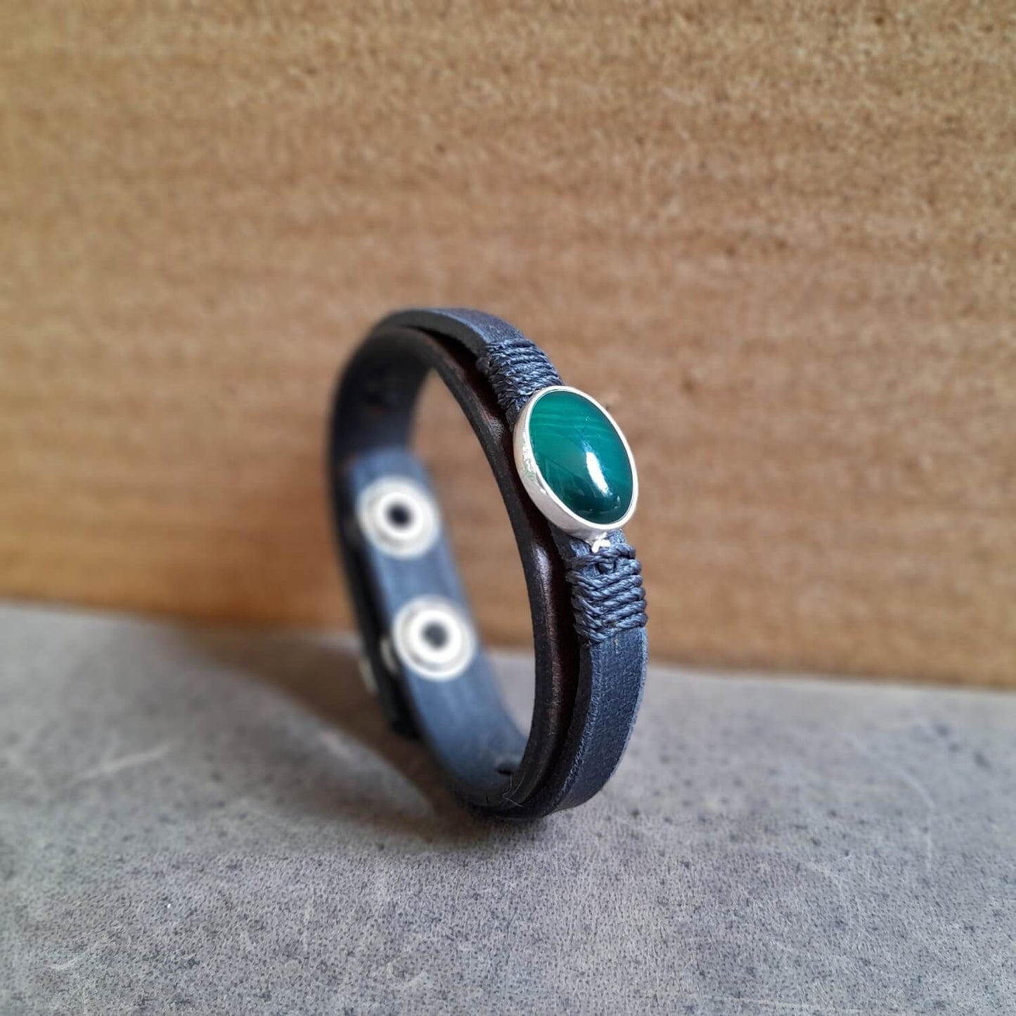 side view of The OOAK Dark Green Aventurine Leather Bracelet: A layered chestnut brown and black full-grain leather bracelet featuring a rare natural dark green aventurine stone on a sterling silver pendant, wrapped with black cord.