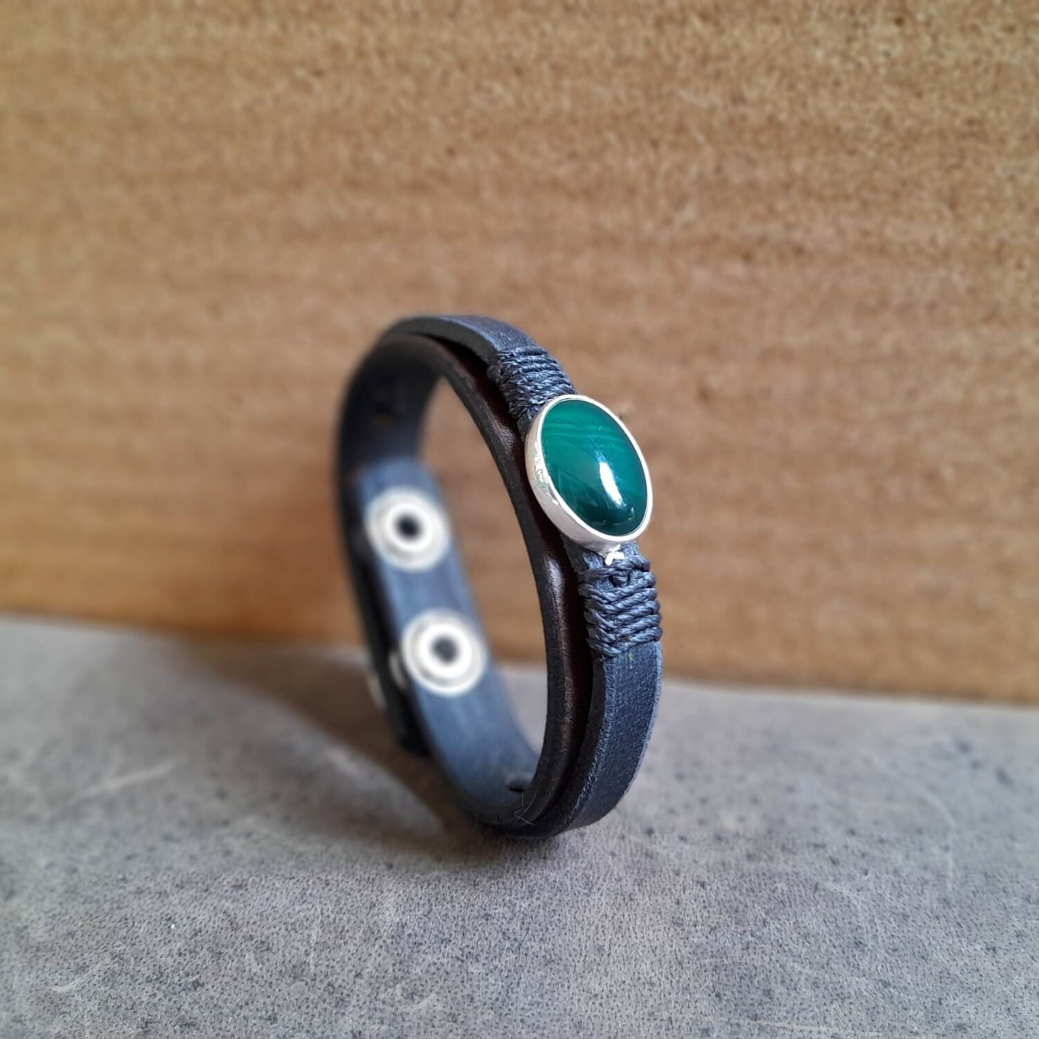 side view of The OOAK Dark Green Aventurine Leather Bracelet: A layered chestnut brown and black full-grain leather bracelet featuring a rare natural dark green aventurine stone on a sterling silver pendant, wrapped with black cord.