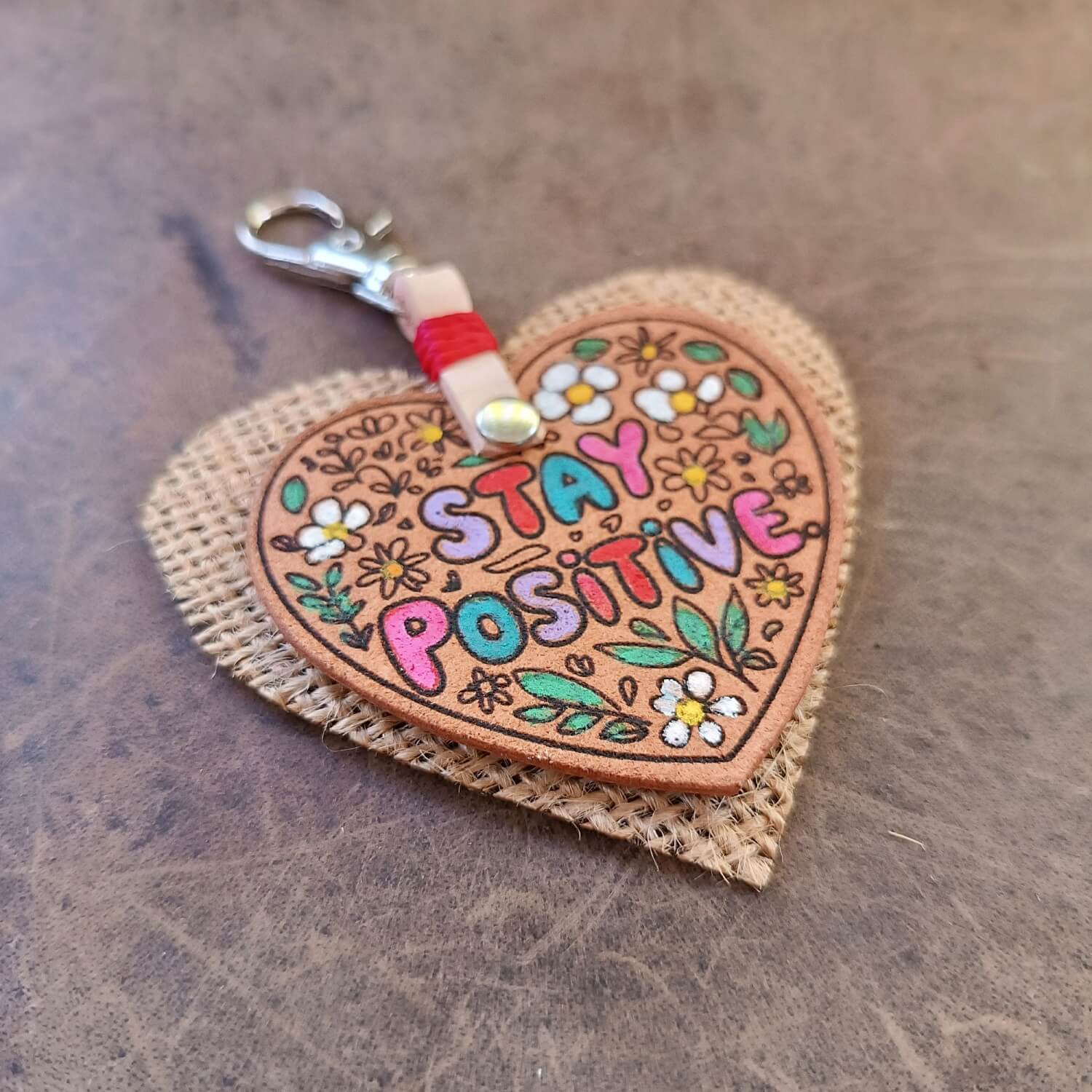 side view of the sleek "Stay Positive" Leather Heart Keychain, focusing on the vibrant hand-painted floral design and "Stay Positive" text in colorful bubble font.