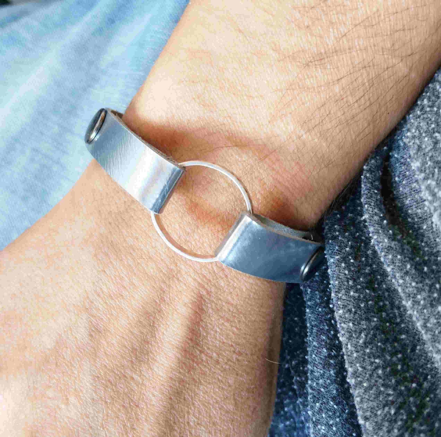 A close-up of a person's wrist wearing a minimalist silver cuff bracelet with a central open circular ring.
