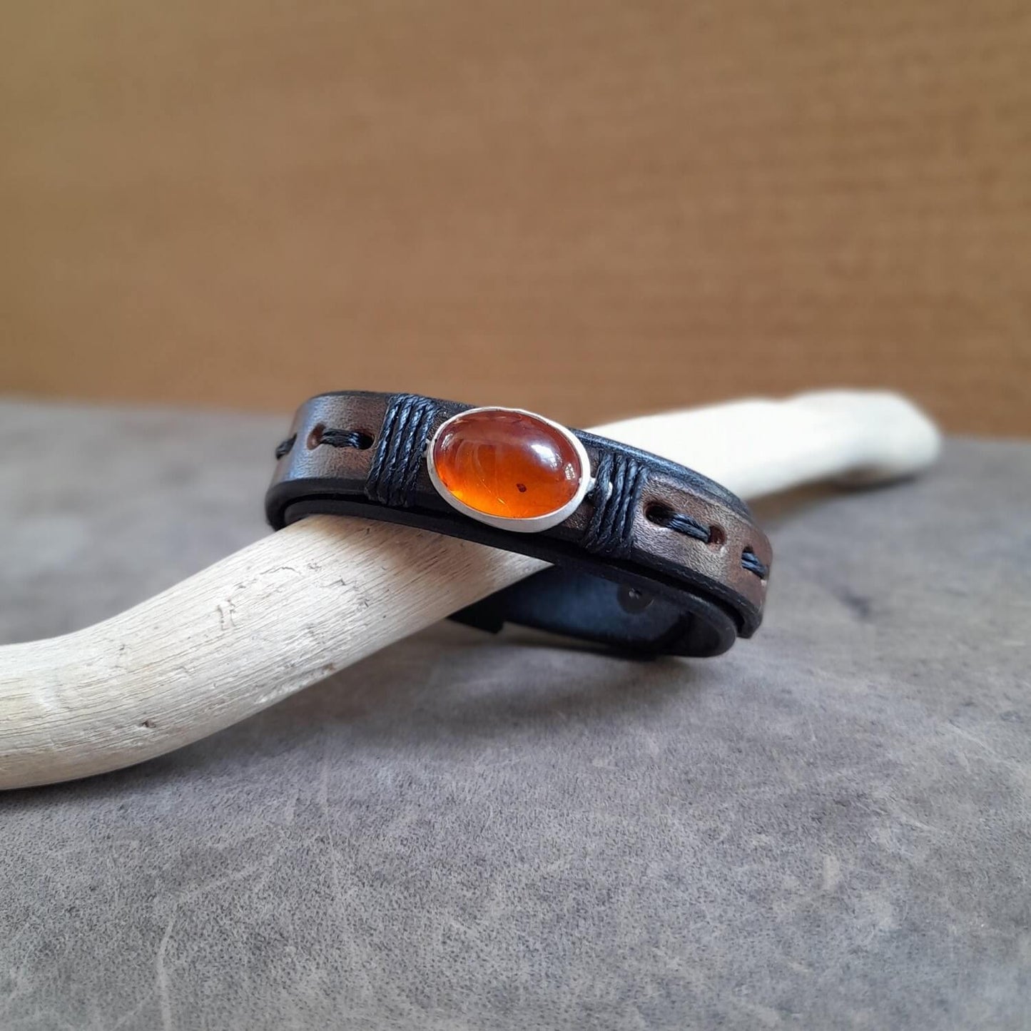 Close-up showing the black oiled Vachetta leather bottom band and the earthy oak brown leather top layer on the Amber Time Capsule Bracelet, with the black cord wrapping the pendant.