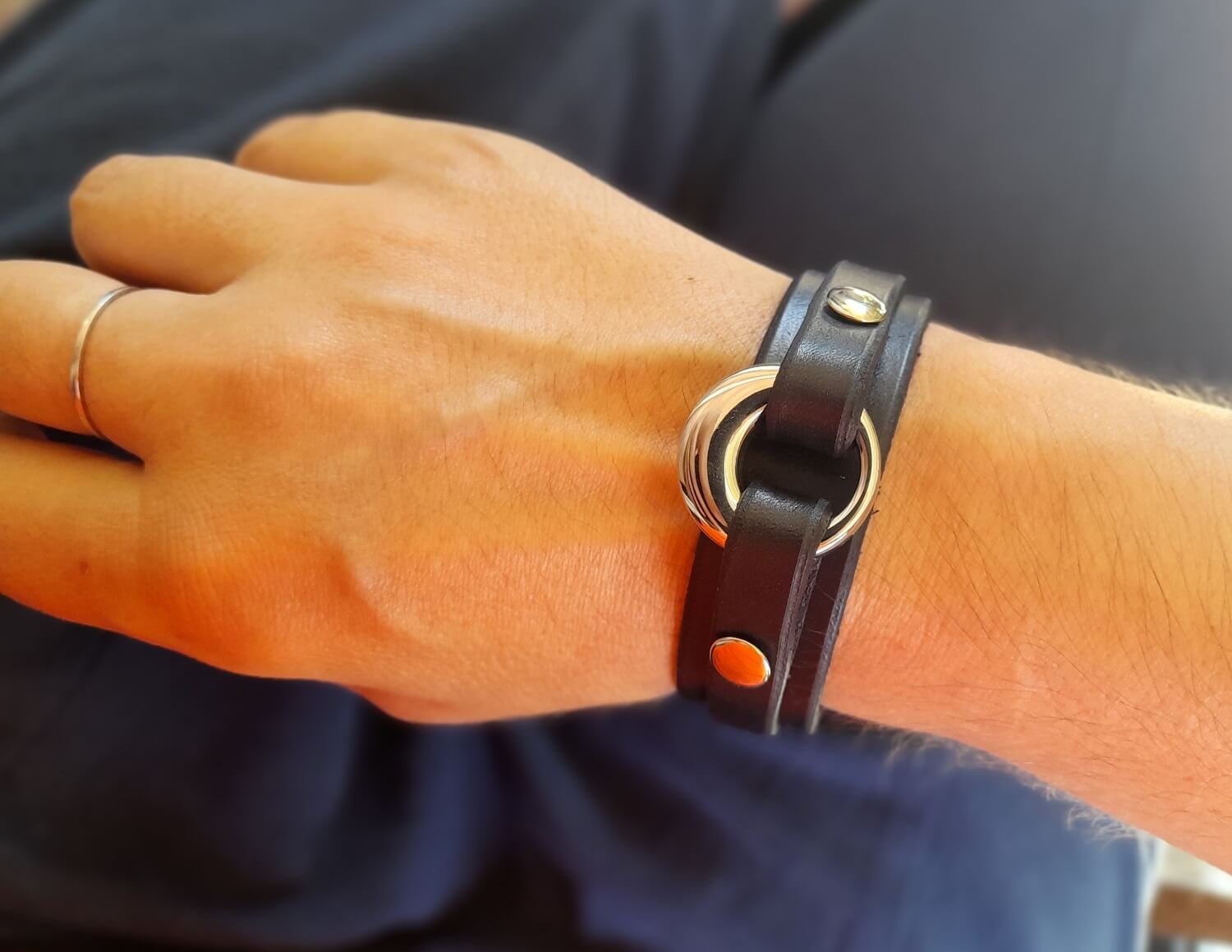 Close-up view of a wrist wearing the black leather bracelet with the silver urn pendant, showcasing its sleek design and casual style.