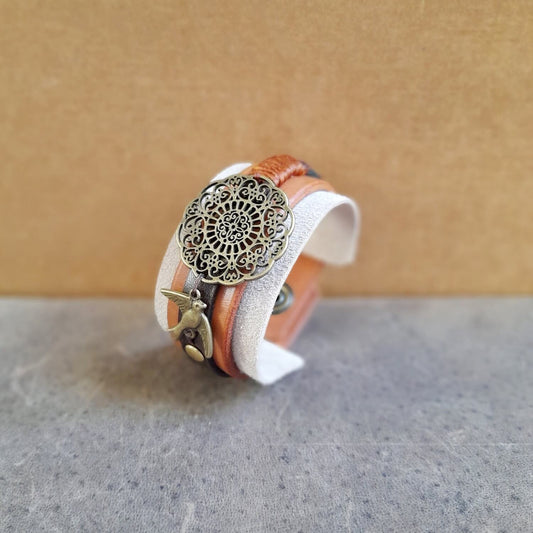The OOAK "Happy Beige" Mandala Cuff, other side view: a wide leather and suede bracelet in neutral, earthy tones, featuring a large antique bronze mandala flower motif and a small bird charm.