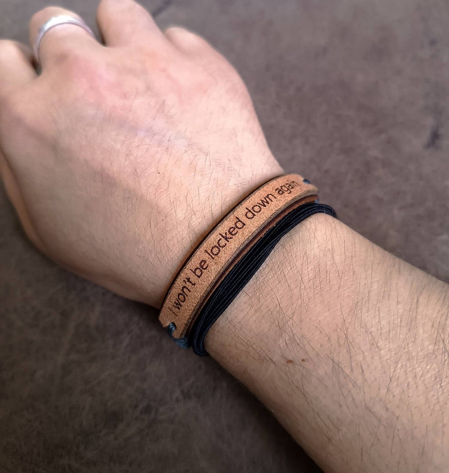 Person wearing a brown leather bracelet with text on a neutral background