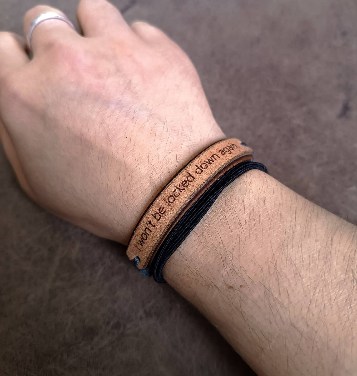 Person wearing a brown leather bracelet with text on a neutral background