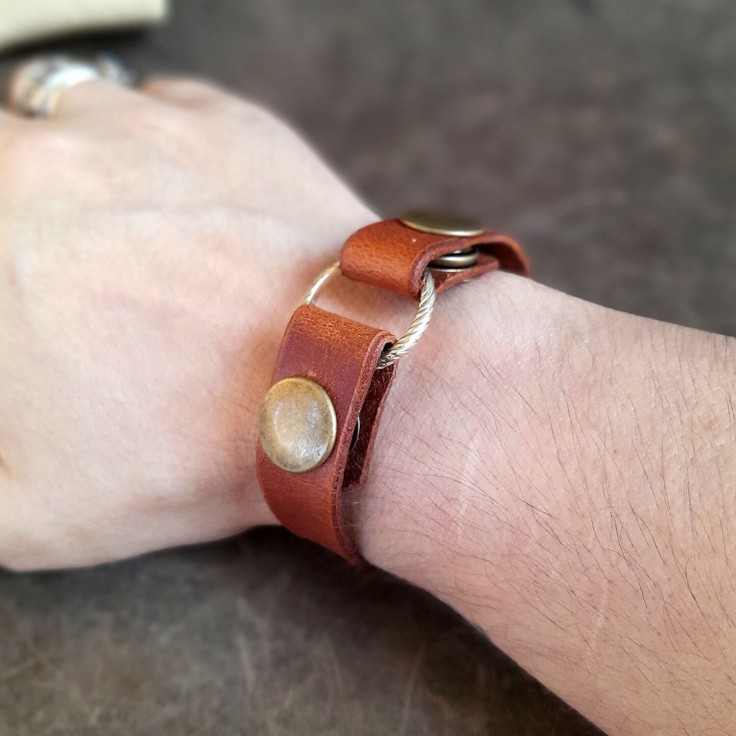 Close-up of a wrist wearing the honey brown brown personalized leather ring holder bracelet securely holding a silver ring, showcasing its comfortable fit and two snap buttons.
