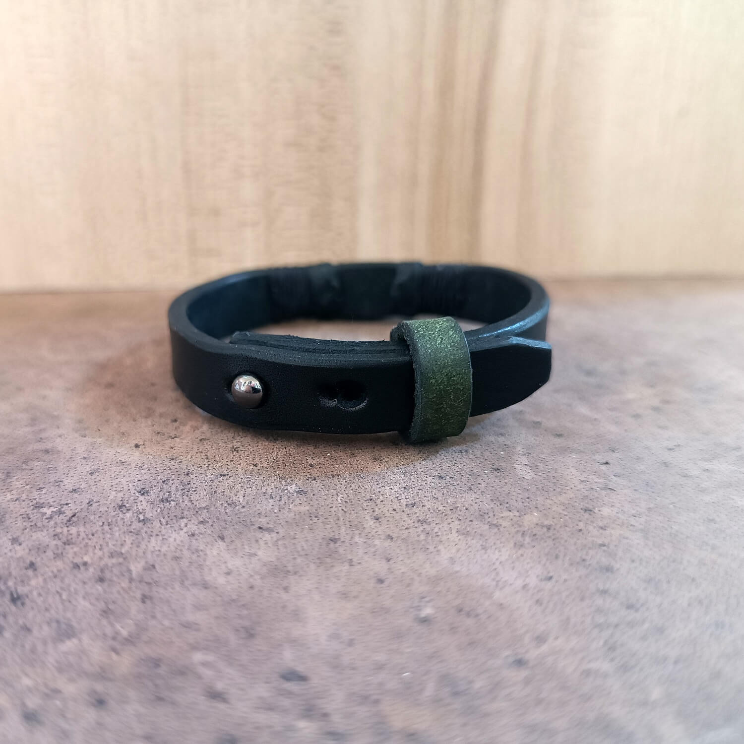 Black leather bracelet with a green accent on a textured surface