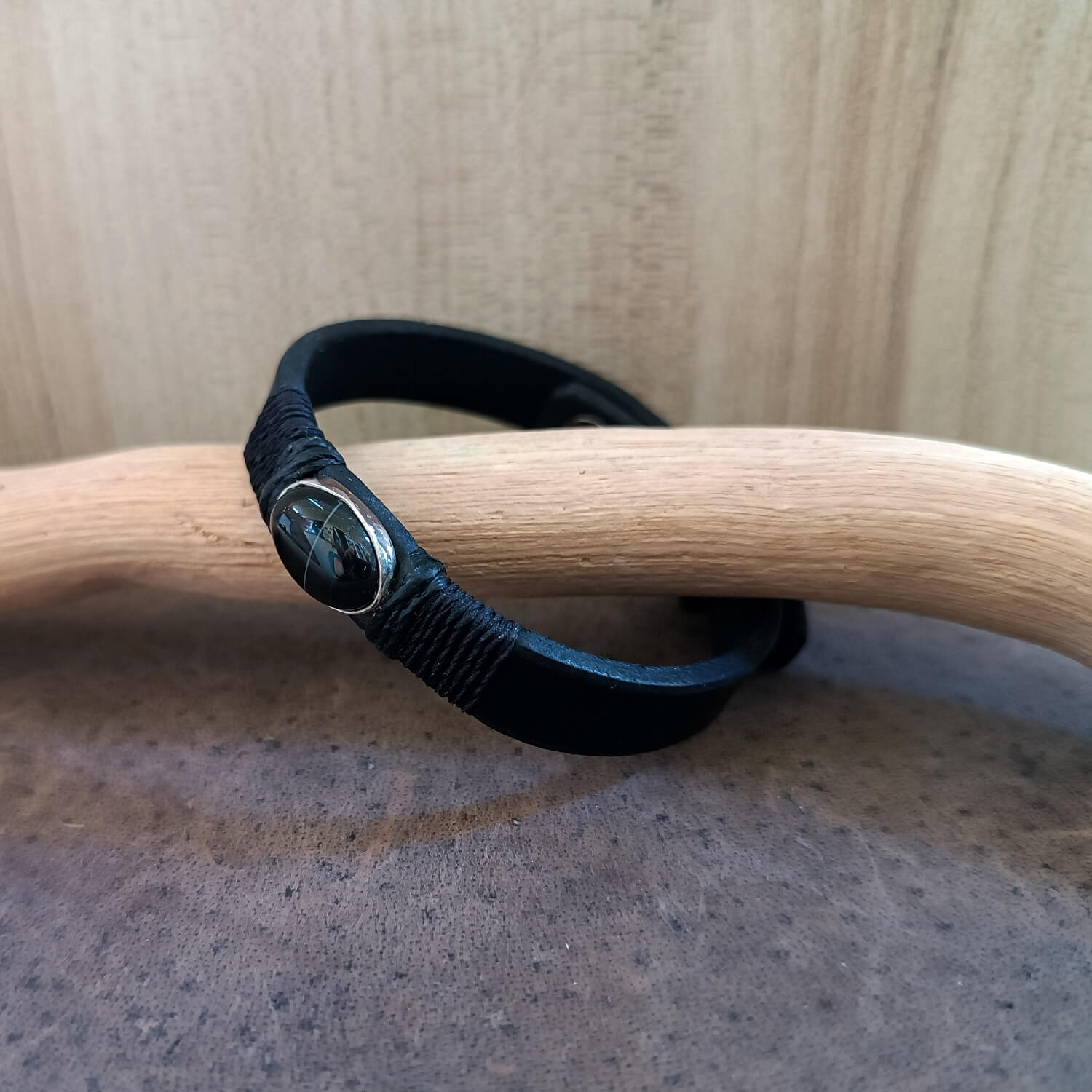 Black leather bracelet with a silver black obsidian pendant against a neutral background