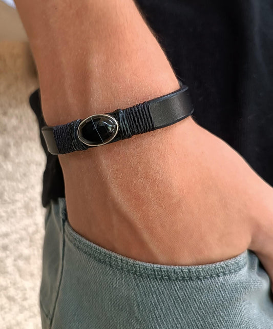 Black leather bracelet with a silver Black Obsidian pendant on a wrist, worn by a man in a casual setting.