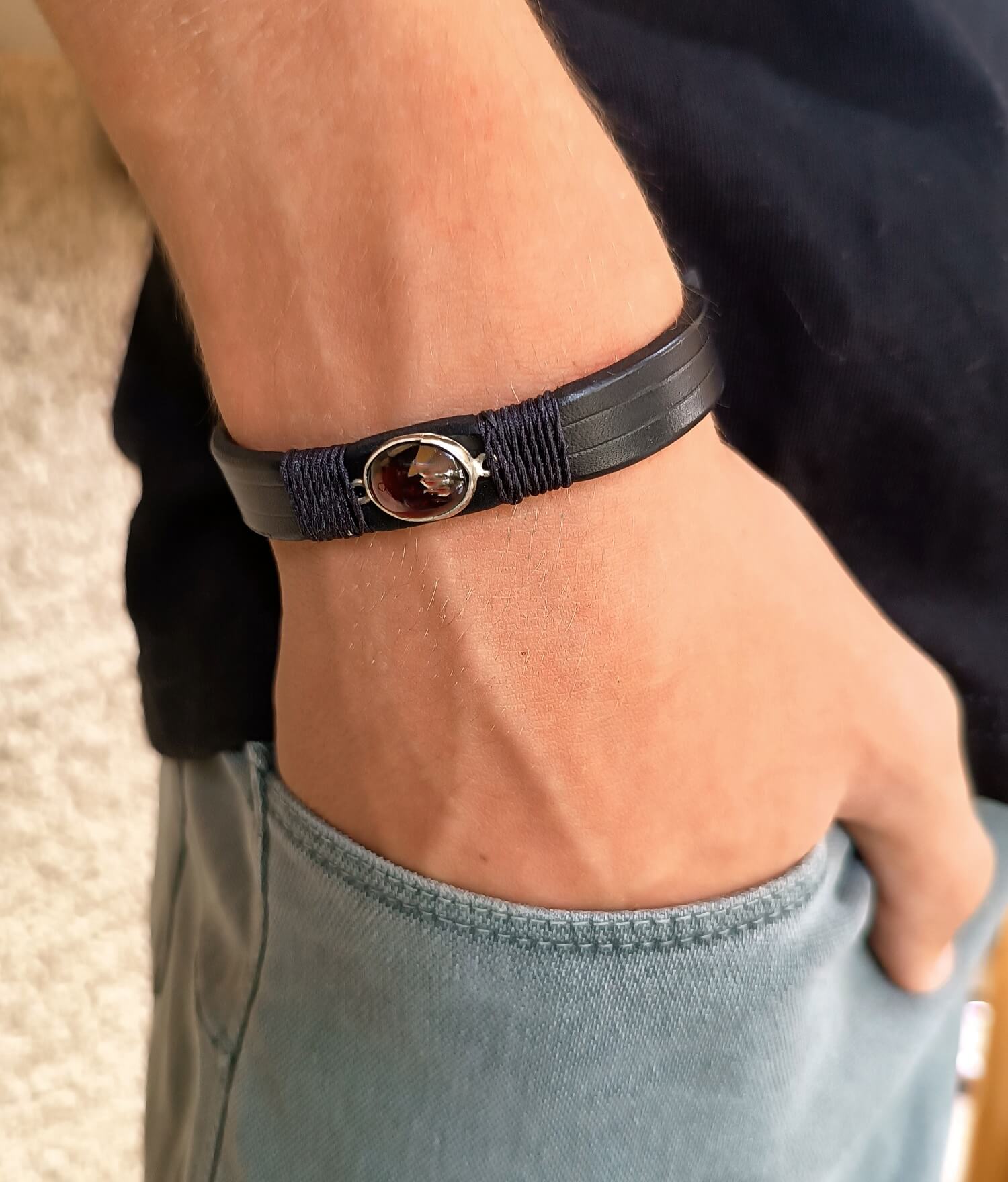Black leather bracelet with a silver 925 red garnet pendant worn on a wrist.
