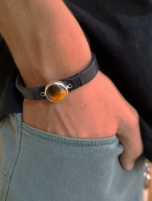 Close-up of a man's wrist wearing a black leather bracelet with a circular Tiger's Eyes stone on sterling silver pendant.