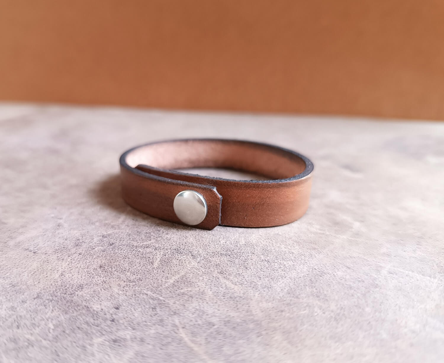 Brown leather bracelet with a silver button clasp showing closure and underside area for secret message engraving.