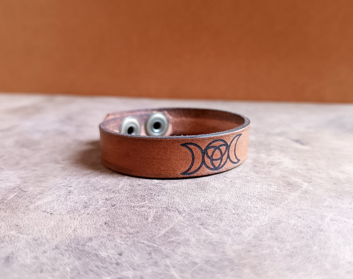 Brown leather bracelet with a triple moon symbol on a textured surface