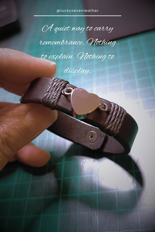 Black leather bracelet with heart urn charm held by a hand on a green cutting mat.