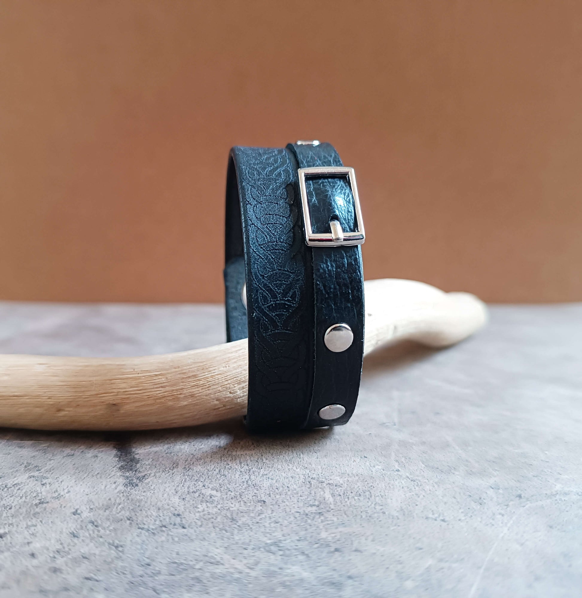 Black leather bracelet with silver buckles on a wooden handle against a brown background