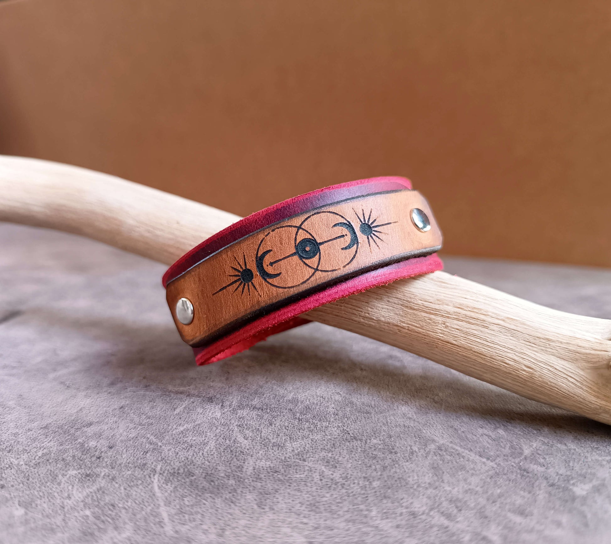 Leather bracelet with star and moon designs on a wooden stick against a brown background
