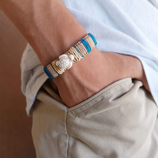 Close-up of a wrist wearing a bracelet with a turtle charm, against a neutral background.