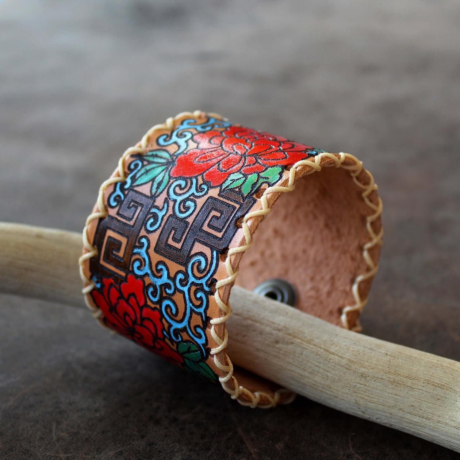 Decorative leather cuff with intricate patterns on a wooden stick.