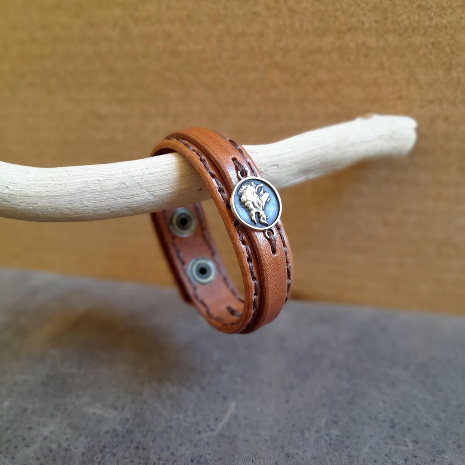 Brown leather bracelet with a wild boar pendant on a wooden stick against a neutral background