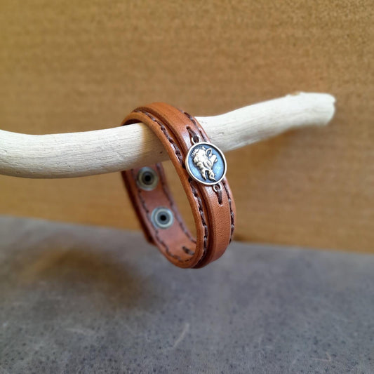 Brown leather bracelet with a wild boar pendant on a wooden stick against a neutral background