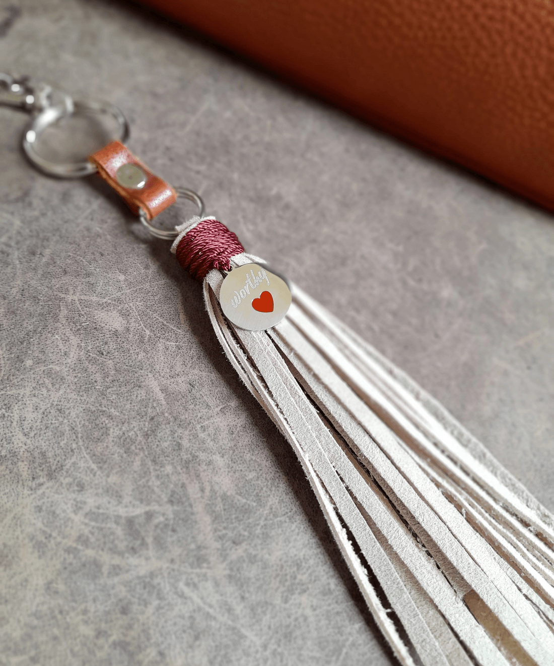 Beige leather tassel keychain with worthy charm on a textured surface