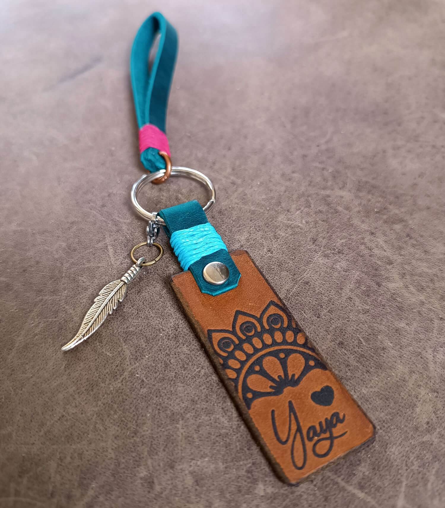 Leather keychain with decorative design and feather charm on a brown surface