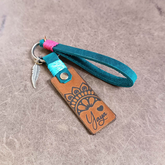 Leather keychain with half mandala design and teal strap on a textured surface