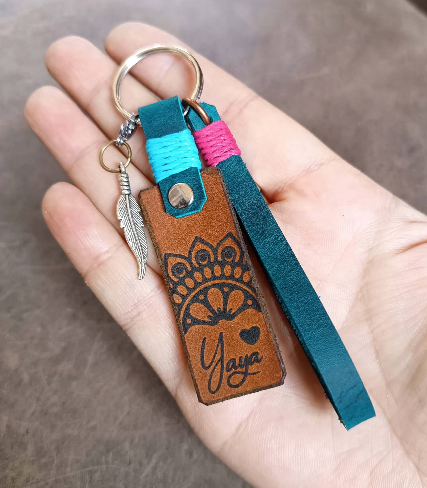 Hand holding a leather keychain with 'Yaya' engraving and colorful strap.