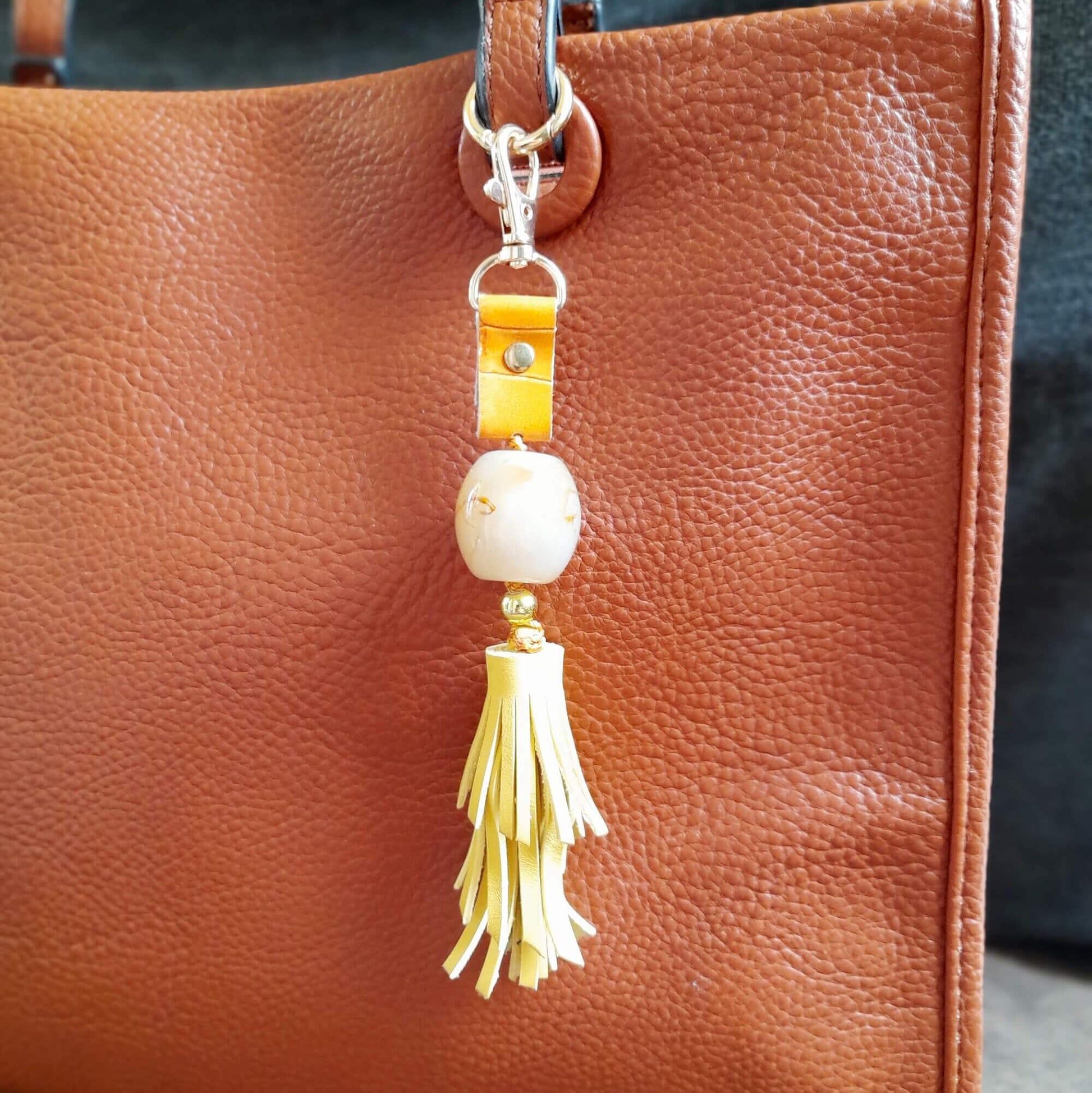 Brown leather handbag with a decorative yellow keychain featuring a yellow tassel and yellow beads.