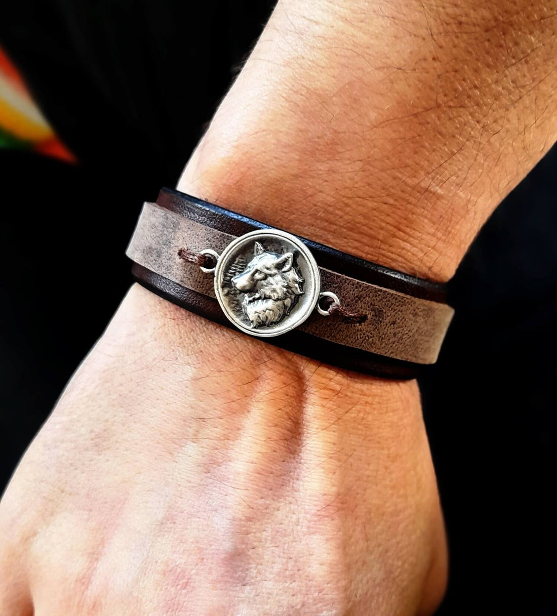 dark brown layered leather bracelet worn on wrist, featuring a handcrafted wolf pendant