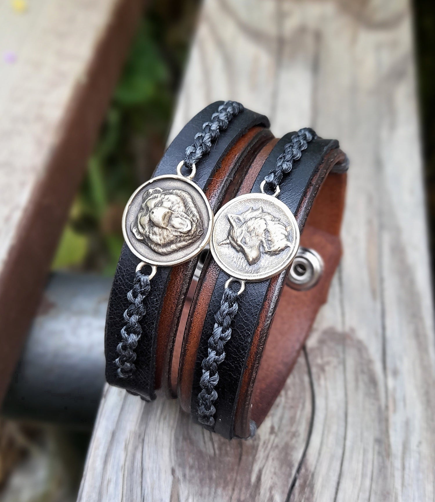 Two handmade leather bracelets on a wooden bench, one featuring a growling bear pendant, and the other a white wolf.