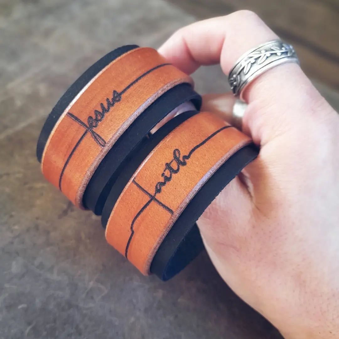 2 handmade leather cuff bracelets, featuring laser engraved "jesus" and "faith" in hand-written calligraphy font