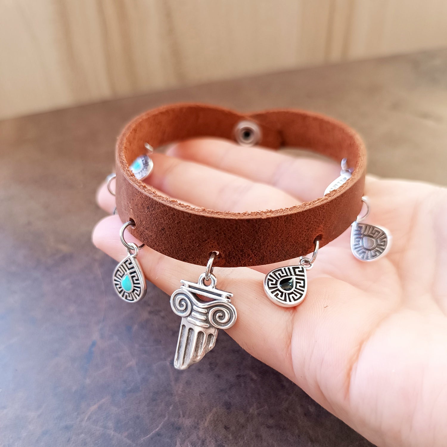 hand holding a handmade leather anklet with silver Greek-themed dangling charms