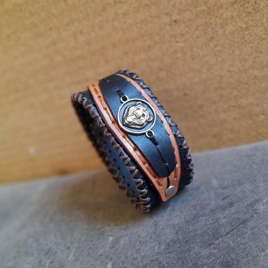 Black Bear leather cuff with brass bear charm on layered black and brown leather.