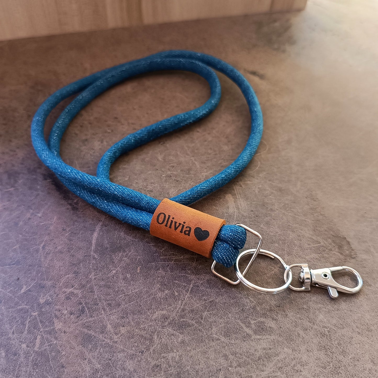 Blue denim lanyard with a brown crazy horse label reading 'Olivia' on a textured surface