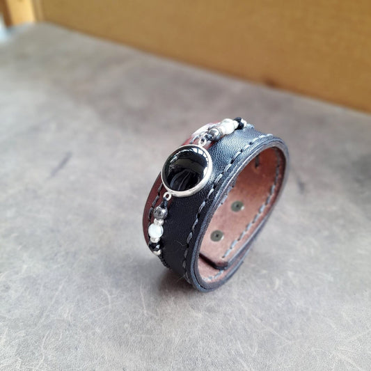 The OOAK Obsidian Power Cuff: A chunky brown Vachetta full-grain leather bracelet with a black asymmetrical top layer, featuring a prominent black obsidian on a polished sterling silver cabochon, and a row of braided hematite, onyx, and smoky quartz beads.