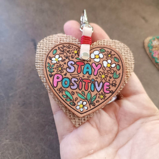 Close-up of the sleek "Stay Positive" Leather Heart Keychain, focusing on the vibrant hand-painted floral design and "Stay Positive" text in colorful bubble font.