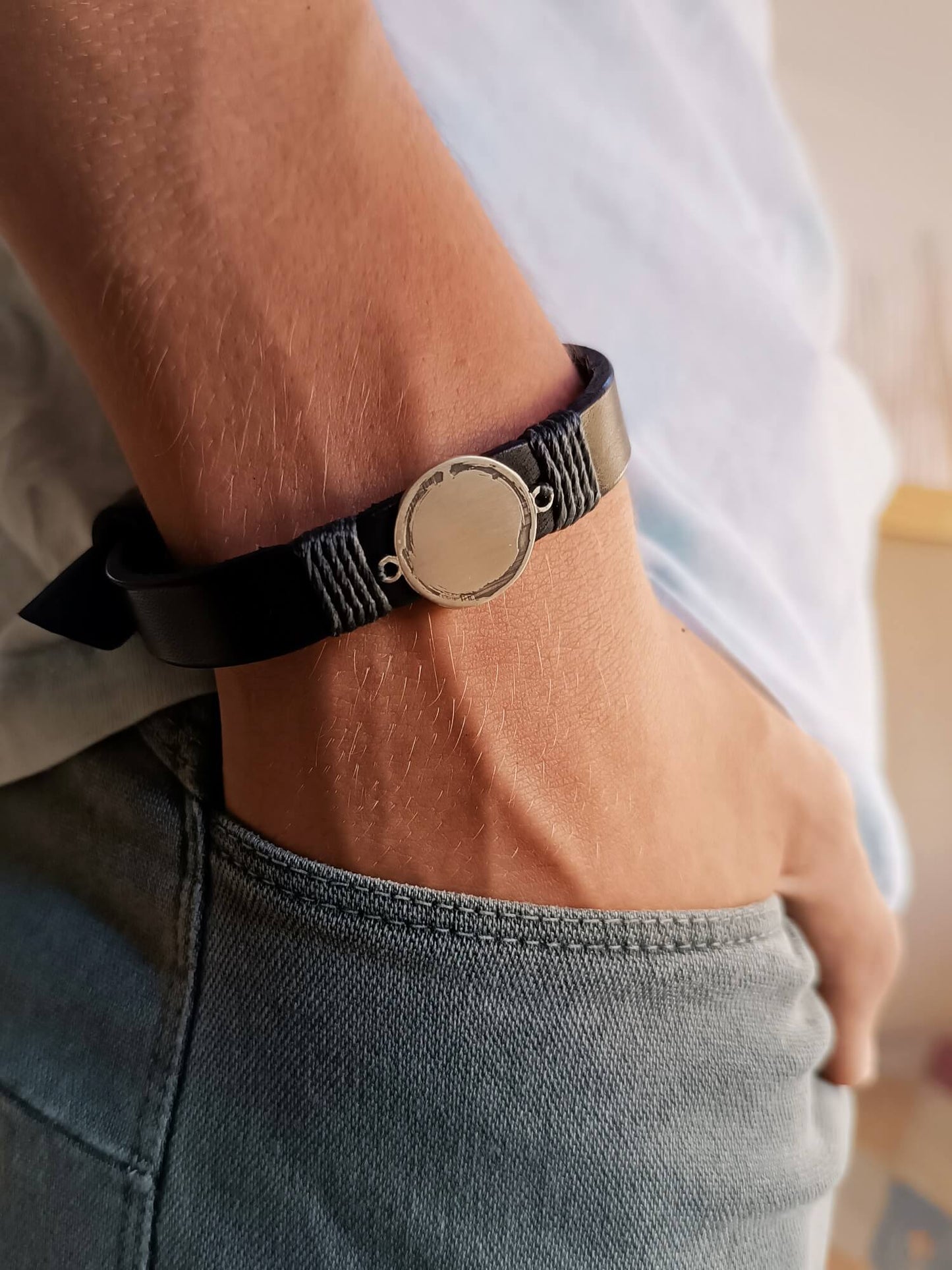 Black leather bracelet with silver Enso Circle pendant on a wrist, worn with a white shirt and jeans.