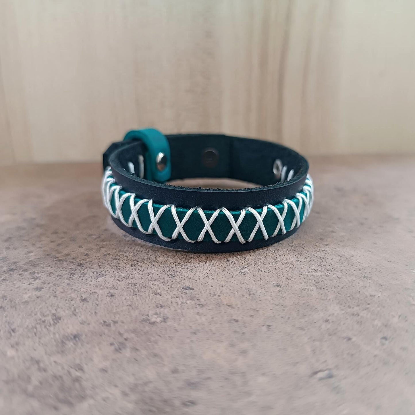 Teal and white braided leather bracelet on a neutral background
