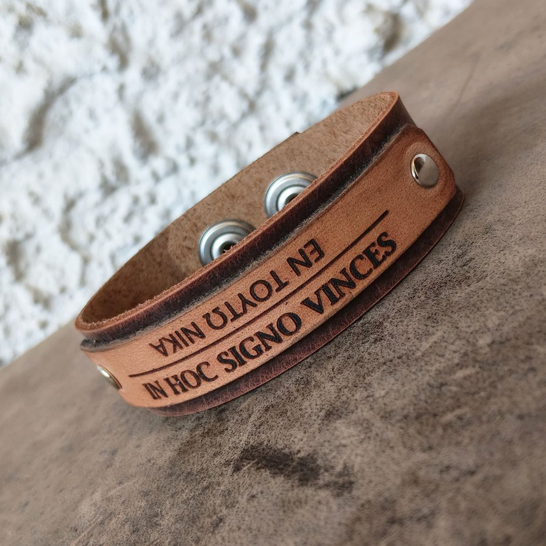 In Hoc Signo Vinces bracelet flat view showcasing engraving and snap closures, photographed on a textured surface.