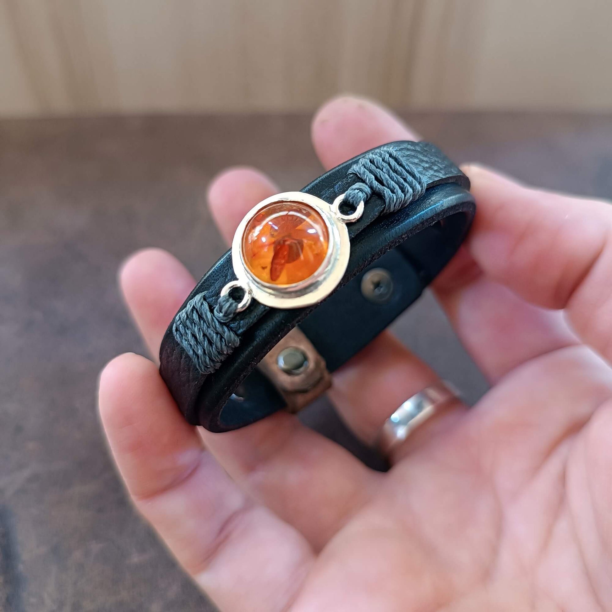 Black leather bracelet with amber stone held in a hand.