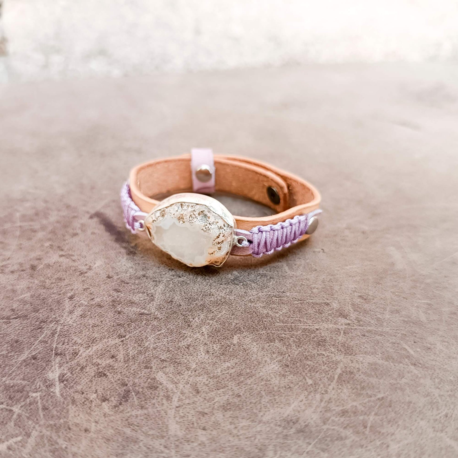 A one-of-a-kind handcrafted leather bracelet featuring a large raw druzy rose quartz set in a handcrafted sterling silver pendant on a slim watchband-style leather cuff.