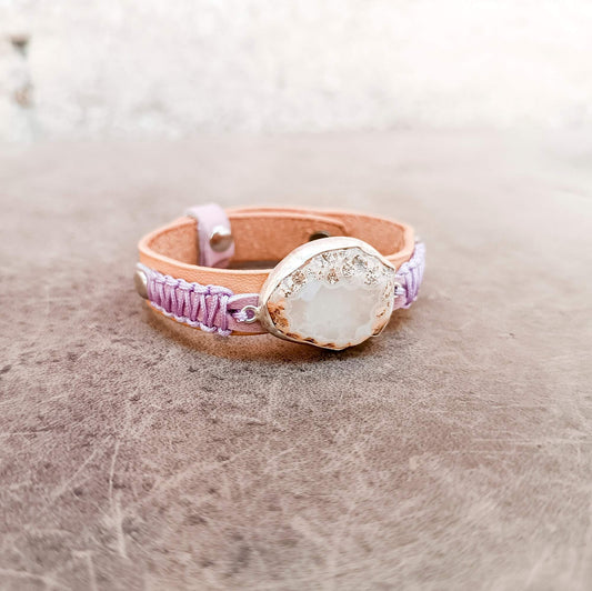 A one-of-a-kind handcrafted leather bracelet featuring a large raw druzy rose quartz set in a handcrafted sterling silver pendant on a slim watchband-style leather cuff.