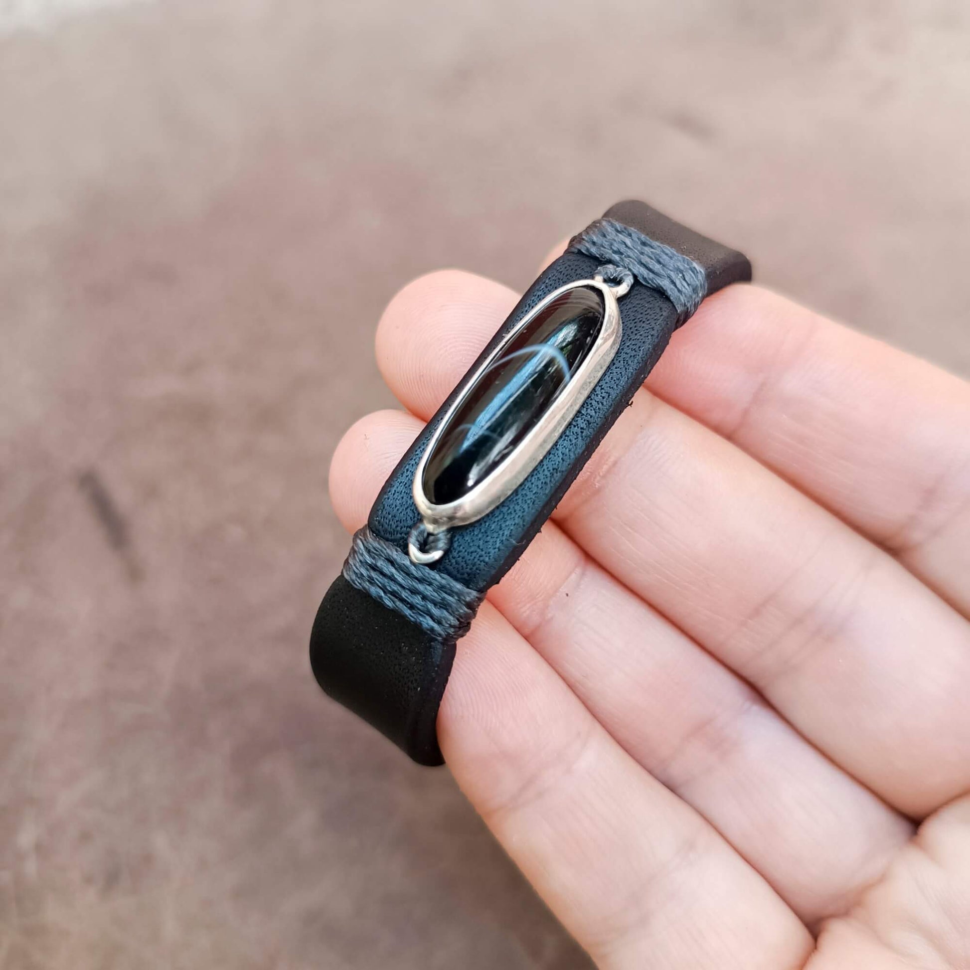 The Eclipse is a one-of-a-kind black obsidian leather bracelet with a handcrafted sterling silver pendant, premium black vachetta leather and unique natural vein, held on hand.