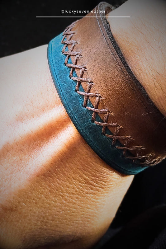 Close-up of a brown leather cuff with blue interior and visible stitching on a person's wrist.