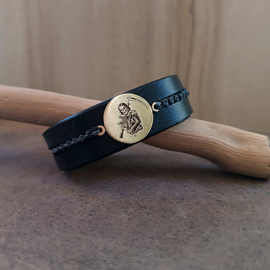 SAMCRO Black leather bracelet with a gold Reaper pendant on a wooden stand
