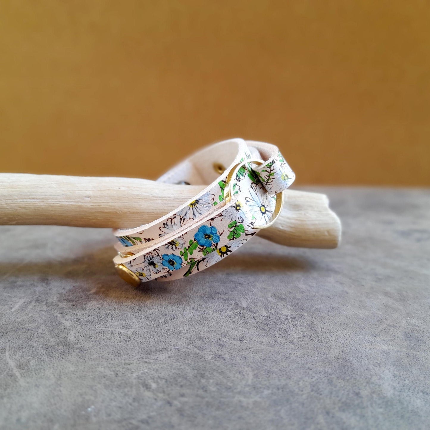 A hand-painted floral leather bracelet with chamomile flowers and forget-me-nots, displayed on a wooden surface.